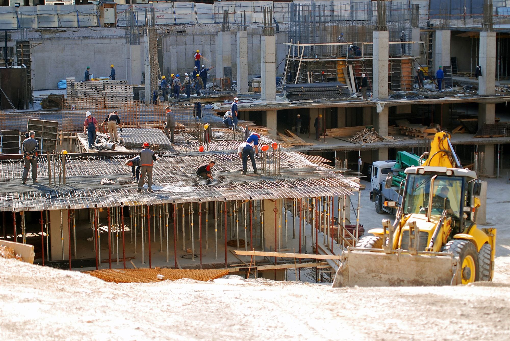 A building crew laying steel reinforcement across a suspended concrete slab on a multi-storey site.