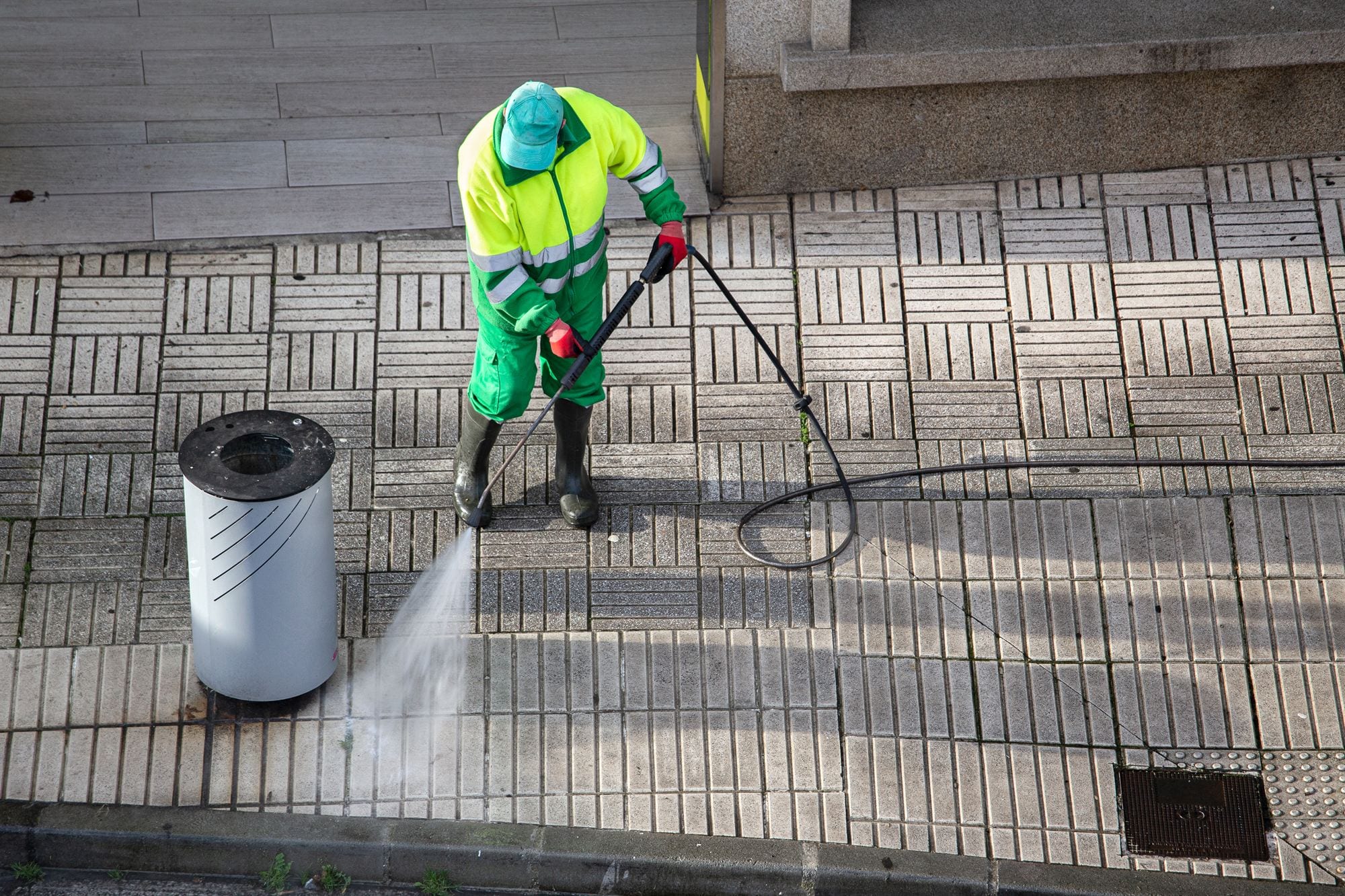 A cleaner in high-vis pressure-washing a paved footpath outside a building.
