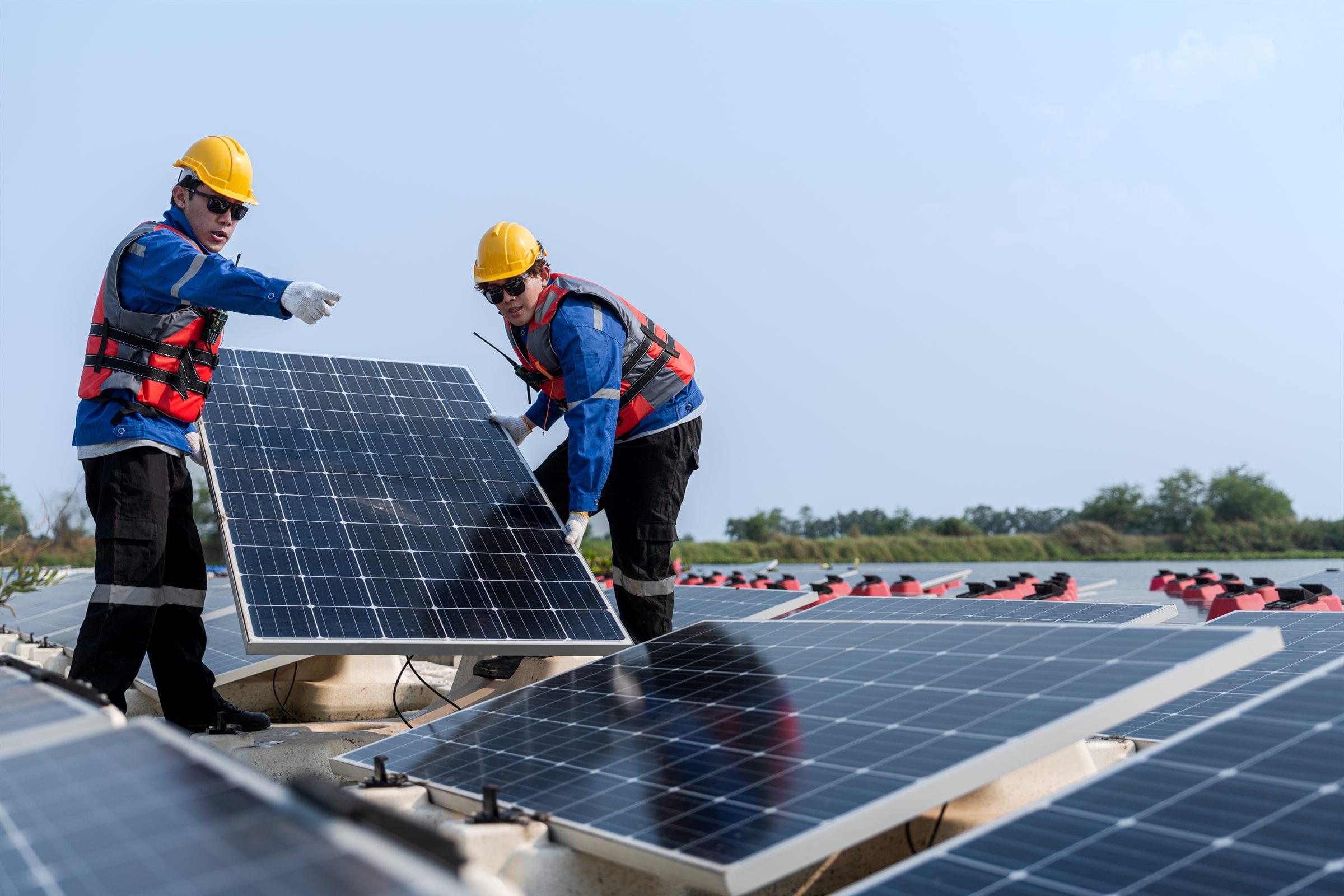 Two technicians in hard hats and high-vis fitting a solar panel on site.